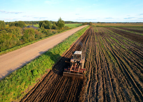 Tactor with disk harrow on plowing field. Cultivated land and soil tillage. Blue Tractor with disc cultivator on land cultivating. Agricultural tractor on soil cultivation field. Plough plowed.