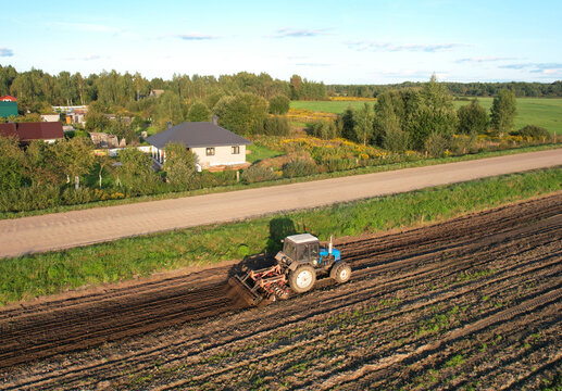 Tactor with disk harrow on plowing field. Cultivated land and soil tillage. Blue Tractor with disc cultivator on land cultivating. Agricultural tractor on soil cultivation field. Plough plowed.