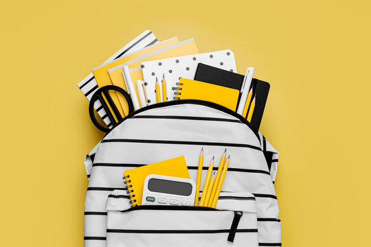 Opened School backpack with stationery on yellow background. Concept back to school. School supplies with white school bag.