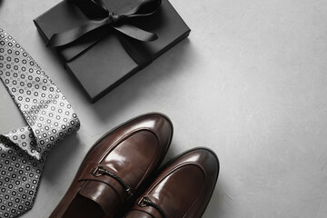 Happy Fathers Day greeting card with gift box. Set of classic mens clothes - brown shoes, tie and gift on gray background. Men's accessories set. Top view. Copy space.