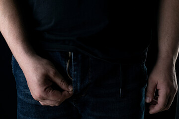 A man's hand unzips his pants in the dark.
