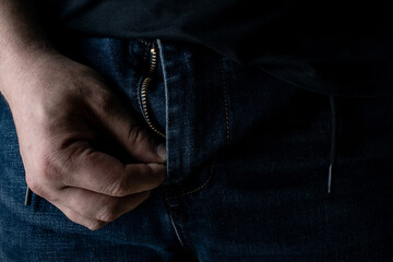 A man's hand unzips his pants in the dark.