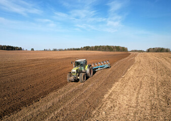 Obraz premium Tractor with plow on soil cultivating. Green tractor plowing field, drone view. Cultivated land and soil tillage. Agricultural tractor on field cultivation. Tractor disk harrow on plowing farm field.