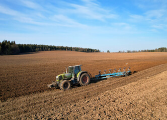 Tractor with plow on soil cultivating. Green tractor plowing field, drone view. Cultivated land and...