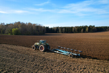 Tractor with plow on soil cultivating. Green tractor plowing field, drone view. Cultivated land and...