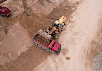 Front end loader on earthworks in quarry. Wheel loader load sand in dump truck in open pit. Heavy...