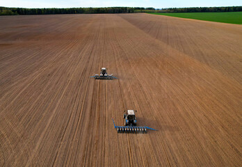 Tractor sowing seed on plowed field. Sowing seeds of corn and sunflower. Blue Tractor with disk...