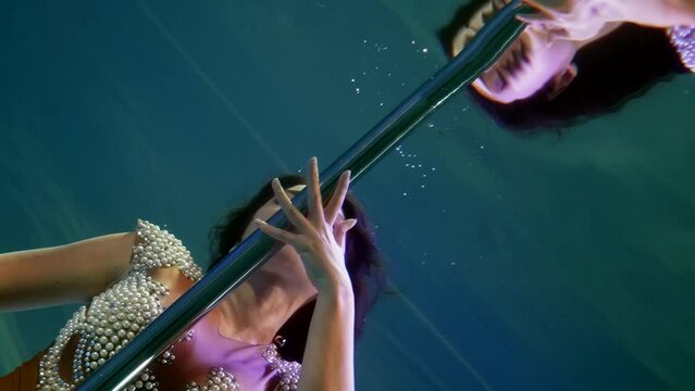 Mysterious dance underwater on a pole of a woman in a pearl dress