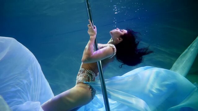 A mermaid woman dances underwater on a pole in slow motion