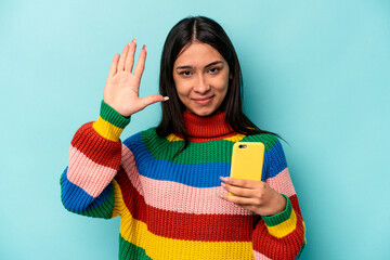 Young caucasian woman holding mobile phone isolated on blue background smiling cheerful showing number five with fingers.