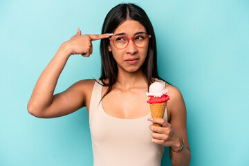 Young hispanic woman holding an ice cream isolated on blue background showing a disappointment gesture with forefinger.