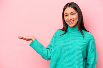 Young hispanic woman isolated on pink background showing a copy space on a palm and holding another hand on waist.