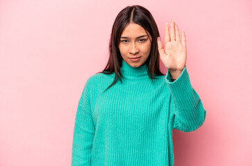 Young hispanic woman isolated on pink background standing with outstretched hand showing stop sign,...