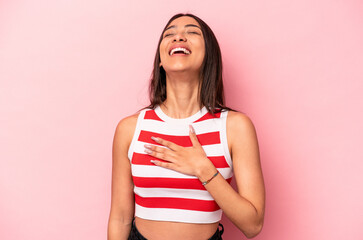 Young hispanic woman isolated on pink background laughs out loudly keeping hand on chest.