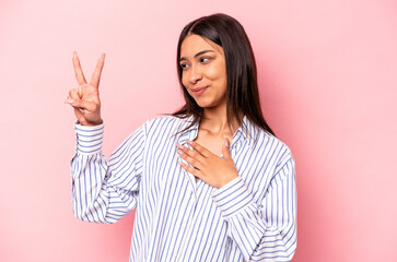 Young hispanic woman isolated on pink background taking an oath, putting hand on chest.