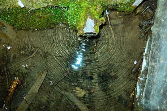 A stream of running water from a forest well creates water ripples at the surface of the lake