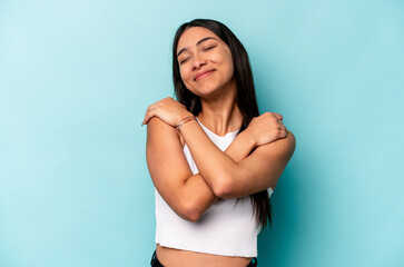 Young hispanic woman isolated on blue background hugs, smiling carefree and happy.