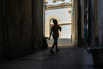 silhoueted boy walking in alleyway on an errand or playing