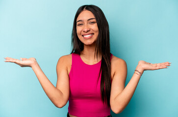 Young hispanic woman isolated on blue background makes scale with arms, feels happy and confident.