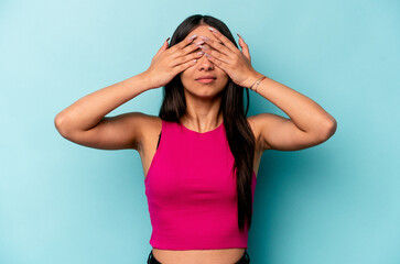 Young hispanic woman isolated on blue background afraid covering eyes with hands.