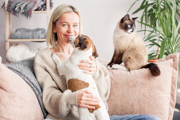 Happy woman playing with her dog on the couch at home - 506422831