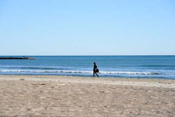 Girl is walking near the sea. Young woman walks along the sand of a beach near Mediterranean Sea against backdrop of waves and a stormy sky at sunset. Female person walks along coastline of the ocean.