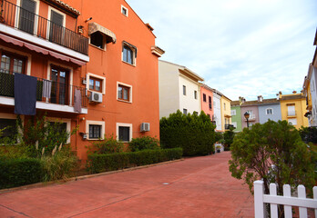 House with palm trees and flowers in yard. Colorful facade and door of the house with apartments at Port Saplaya. Landscape design at suburb home. Garden with flowers near house on street courtyard..