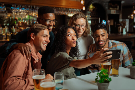 Mixed group of young adults sitting in restaurant taking selfies with cellular device