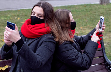 two female friends take a selfie on the phone while sitting on a park bench