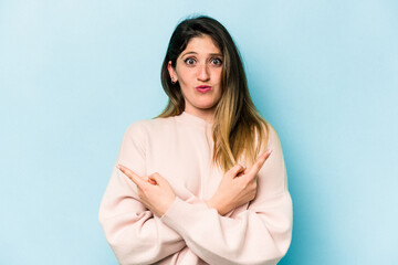 Young caucasian woman isolated on blue background points sideways, is trying to choose between two options.