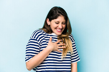 Young caucasian woman isolated on blue background laughing keeping hands on heart, concept of happiness.
