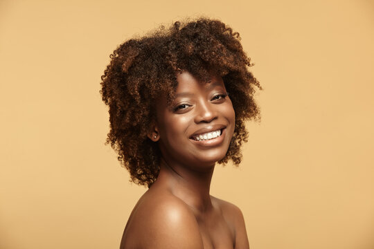 Portrait of African American woman with a clean healthy skin on a beige isolated background. Smiling beautiful black female model.