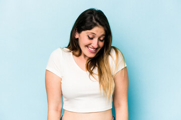 Young caucasian woman isolated on blue background laughs and closes eyes, feels relaxed and happy.