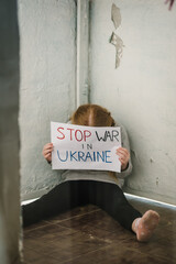 Little upset child calls No War, raises banner with inscription Stop war in Ukraine. Kid sits on...