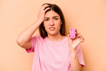 Young hispanic woman holding a keys car isolated on beige background being shocked, she has remembered important meeting.