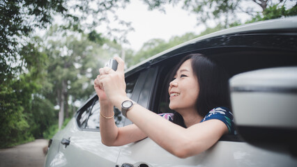 Happy asian woman taking photo and looking out of car with smile and relax.Concept of travel and transportation