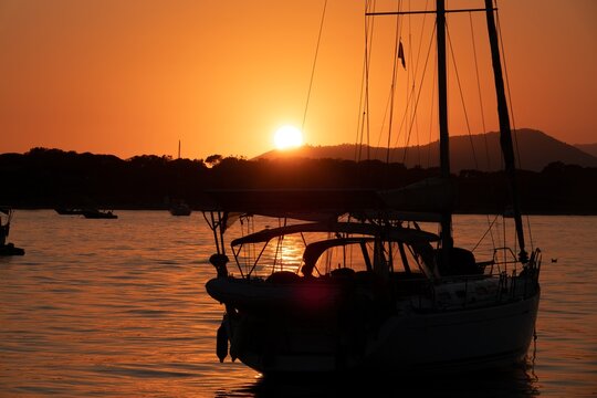 A white sailboat sails on the sea with an orange sunset