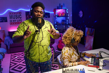 Modern gen Z African American man rapping while recording song in home studio, his girlfriend...