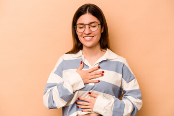Young hispanic woman isolated on beige background laughs happily and has fun keeping hands on stomach.