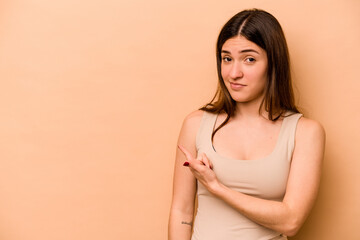 Obraz premium Young hispanic woman isolated on beige background smiling and pointing aside, showing something at blank space.