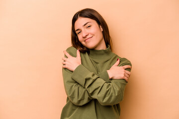 Young hispanic woman isolated on beige background hugs, smiling carefree and happy.