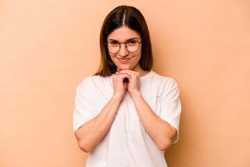 Young hispanic woman isolated on beige background keeps hands under chin, is looking happily aside.