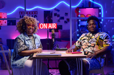 Portrait of modern young gen Z African American influencers sitting at desk in broadcasting studio...