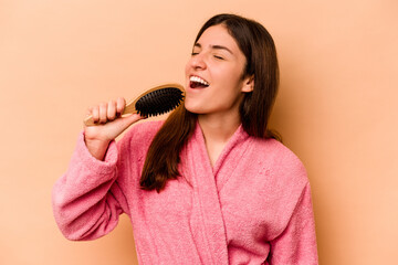 Young hispanic woman holding hairbrush isolated on beige background