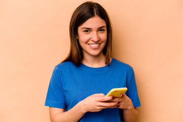 Young caucasian woman holding mobile phone isolated on beige background