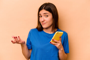 Young caucasian woman holding mobile phone isolated on beige background