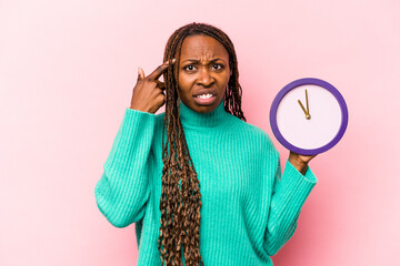 Young African American woman holding a clock isolated on pink background showing a disappointment...