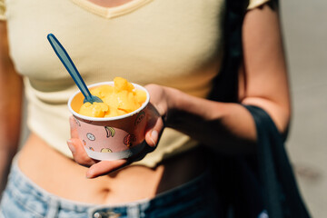 Close up of teen girl with paper cup with mango yellow sorbet ice cream on sunny summer day - obrazy, fototapety, plakaty