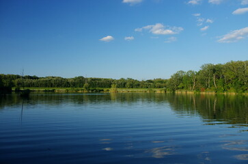Natural panorama with lake and blue sky. Clouds in Lake Country. Summer panorama with green trees by the lake, beautiful and colorful reflections of trees, blue sky and clouds in the in the water.	