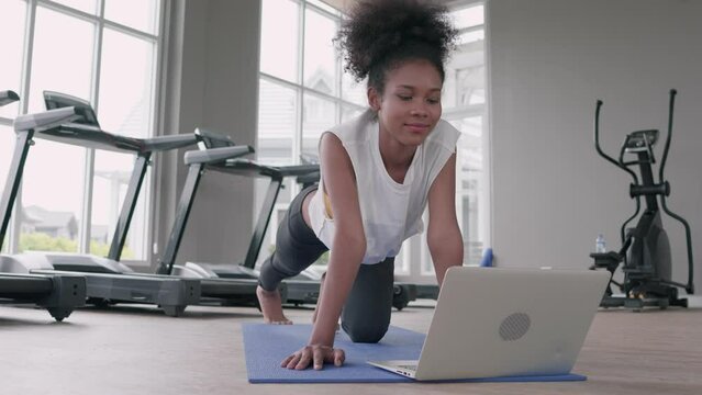 Fitness young black woman doing exercise yoga in gym. African american female loook at laptop computer lesson practicing Yaga plank pose on social online internet class. Healthy lifestyle concept.